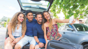 Group of teenagers on a road trip, sitting on the tailgate of a vehicle taking a selfie