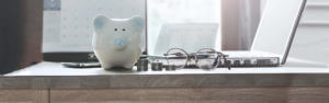 Piggy bank a pair of glasses and a laptop with some coins in stacks