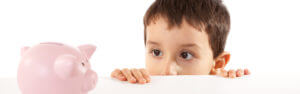 Small boy peeking over a counter top at a piggy bank