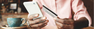 A man in a coffee shop with his debit card and his mobile phone