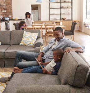 Father And Son Sit On Sofa In Lounge Using Digital Tablet