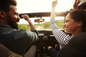 Happy couple driving in their car with arms in the air