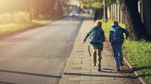 Two school boys running on sidewalk on way to school. Sunny day morning.