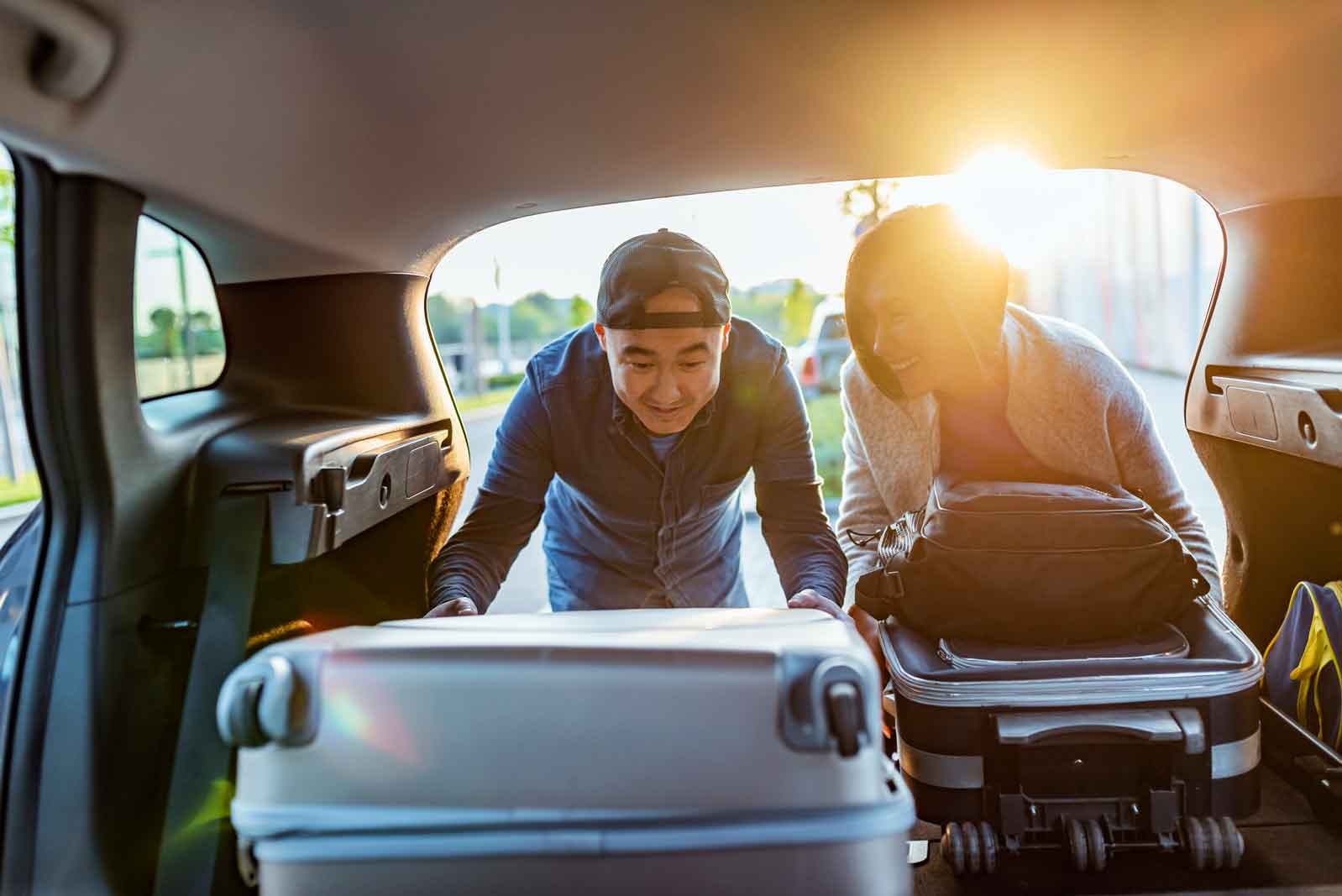 End Of The Trip Close-up Of Asian Couple Putting Luggage In A Car Trunk during the day. The young couple helping each other unloading luggage. Portrait of the Asian family putting a suitcase into the car trunk, ready for a holiday together. Happy Asian young man and woman with their suitcase put in the car trunk. preparing for vacation.