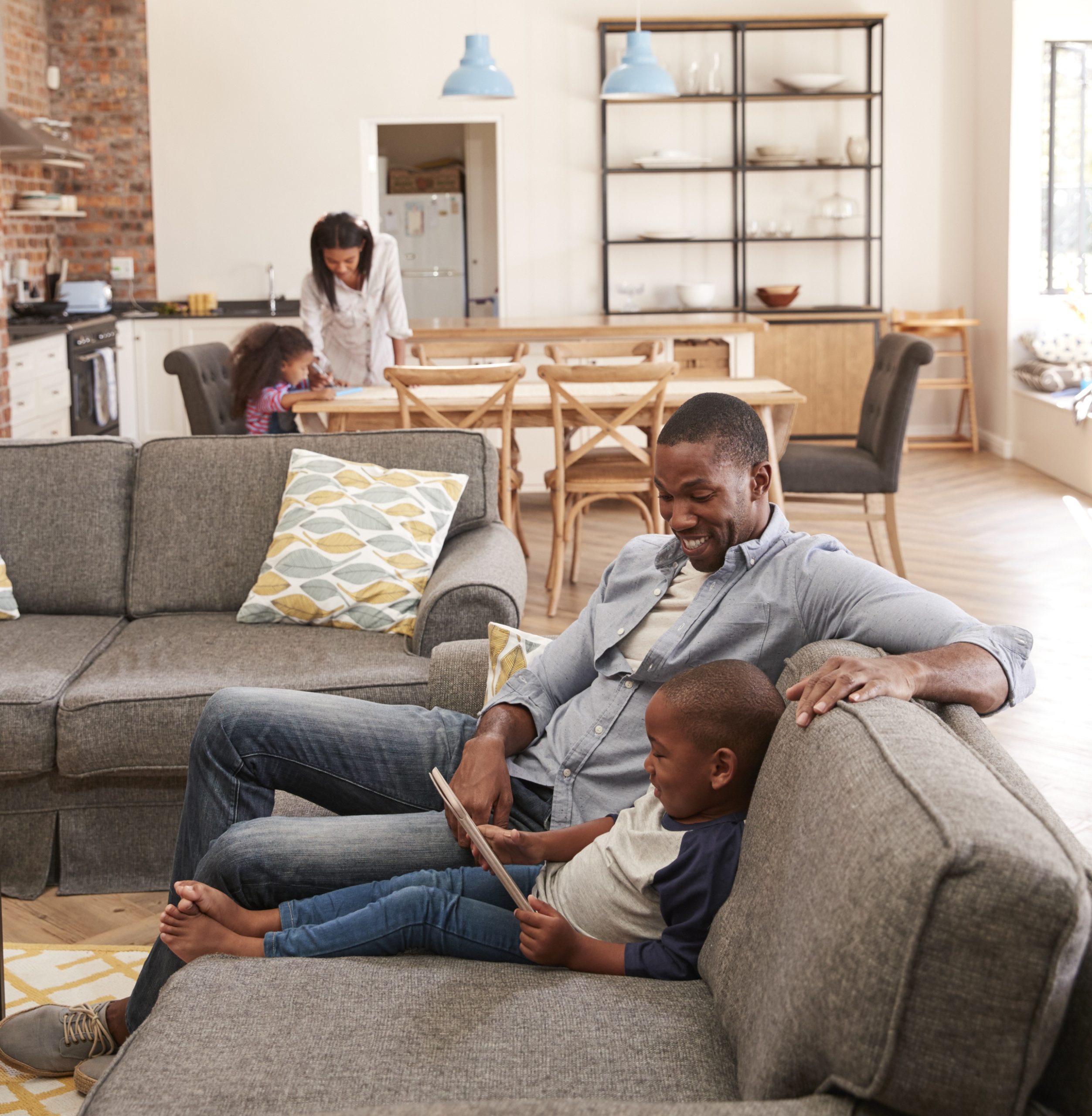 Father And Son Sit On Sofa In Lounge Using Digital Tablet