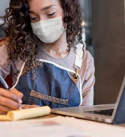 Woman wearing mask and apron while writing down notes