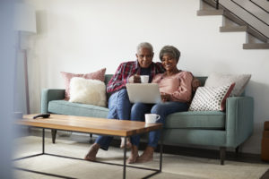 Senior Couple Sitting On Sofa At Home Using Laptop To Shop Online