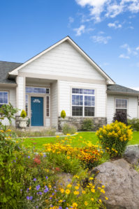 New home with gorgeous flower garden. Peaked roof; blue sky.