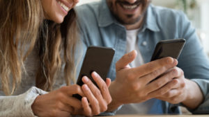 Close up happy family couple using smartphones, sharing contacts or funny content, watching photos or videos or enjoying online banking