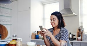 Woman Slightly Smiling Holding Phone In Kitchen Side