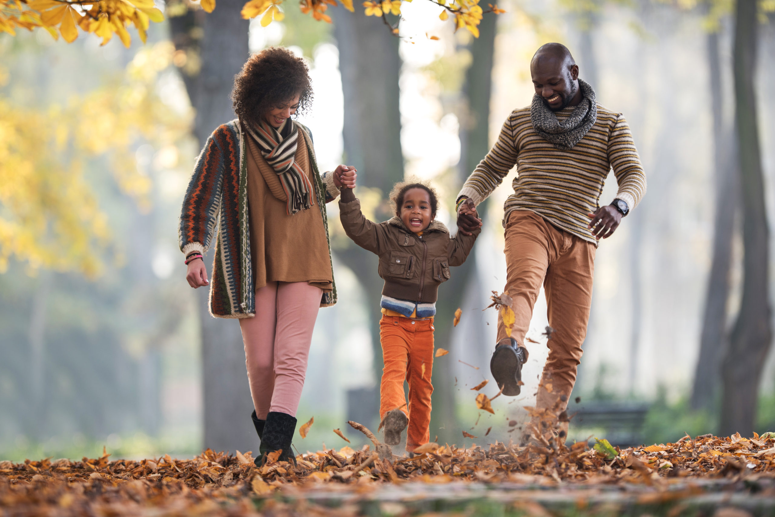 Happy African American family having fun while walking in nature during autumn season.