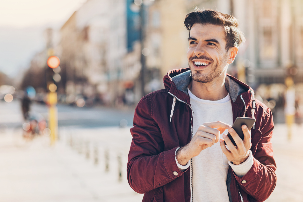 Young man with smart phone texting outdoors in the city