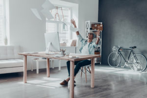 Handsome young man throwing paper in air and smiling while sitting at his working place in creative office