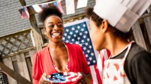Young Chef, African American boy interacting with his mother while setting up a BBQ grill for outdoor 4th July backyard celebration.