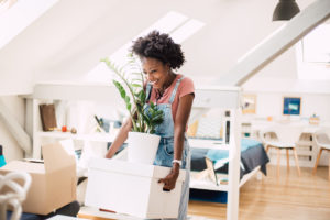 Beautiful African-American young woman carrying her belongings while moving into the new home.