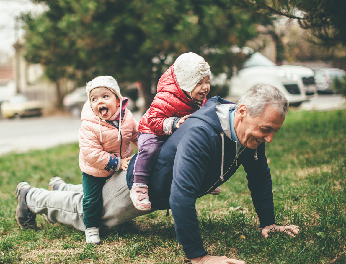 We Exercise Togather A photo of a playful grandfather and granddaughter. They are casually dressed and playing in the park. They exercise together. A grandfather is exercising while granddaughters are sitting on his back.