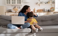 Millennial mother, successful businesswoman bonding with preschool son on covid-19 lockdown happy to work remote. Young woman hug cute little kid playing games on tablet with laptop computer in hands