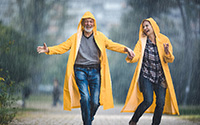 Happy Mature Couple In Raincoats Having Fun On A Rainy Day At The Park.