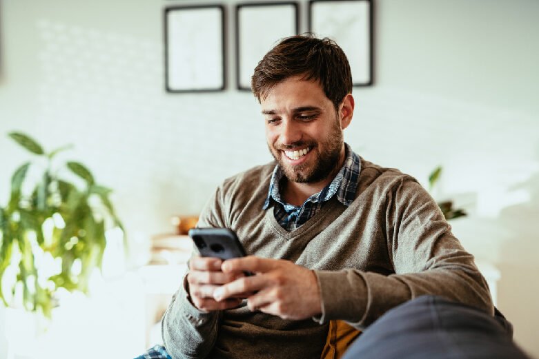 Man Smiling While Using Phone To Complete Digital Banking Task