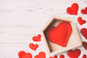 Top View Of Red Heart In A House Decorated With Small Hearts On Wooden Background. Valentine's Day. Home Sweet Home Concept