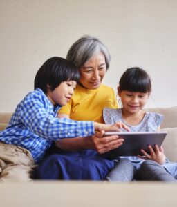 A Taiwanese grandmother reads from an electronic tablet to her grandchildren in a home.