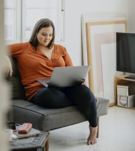 Mid-size woman sitting in the living room and reading on her laptop.