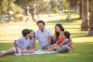 Family sitting in a park on a picnic blanket.