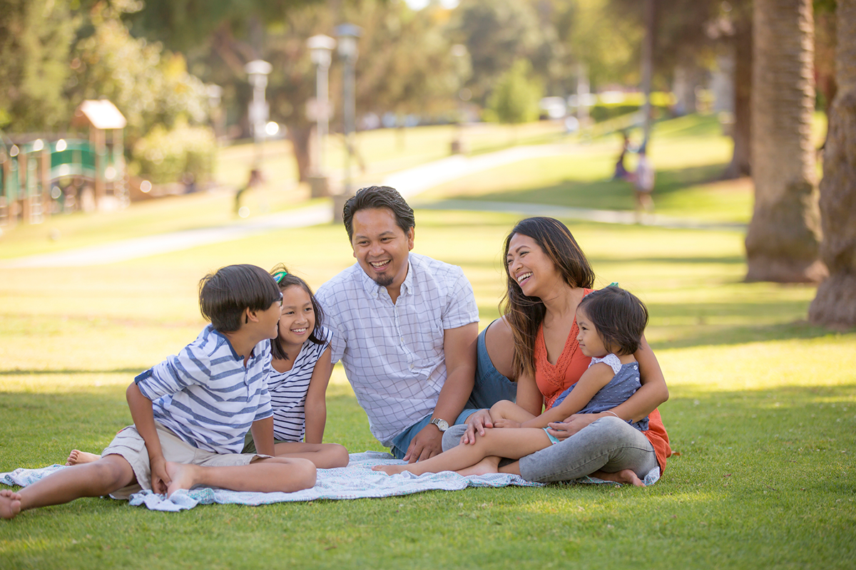 IStock 589425198 Family sitting in a park on a picnic blanket.