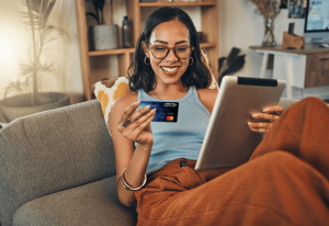 Woman happily sitting at home with tablet and credit card
