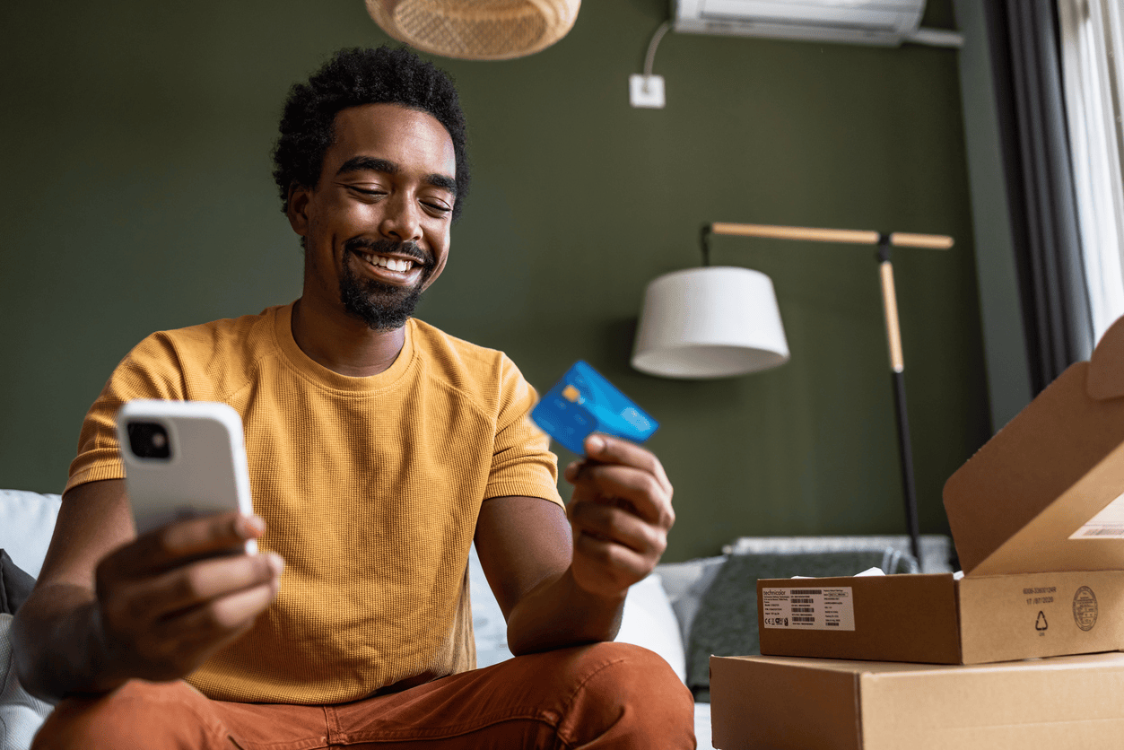 Smiling man at home looking at debit card and holding phone