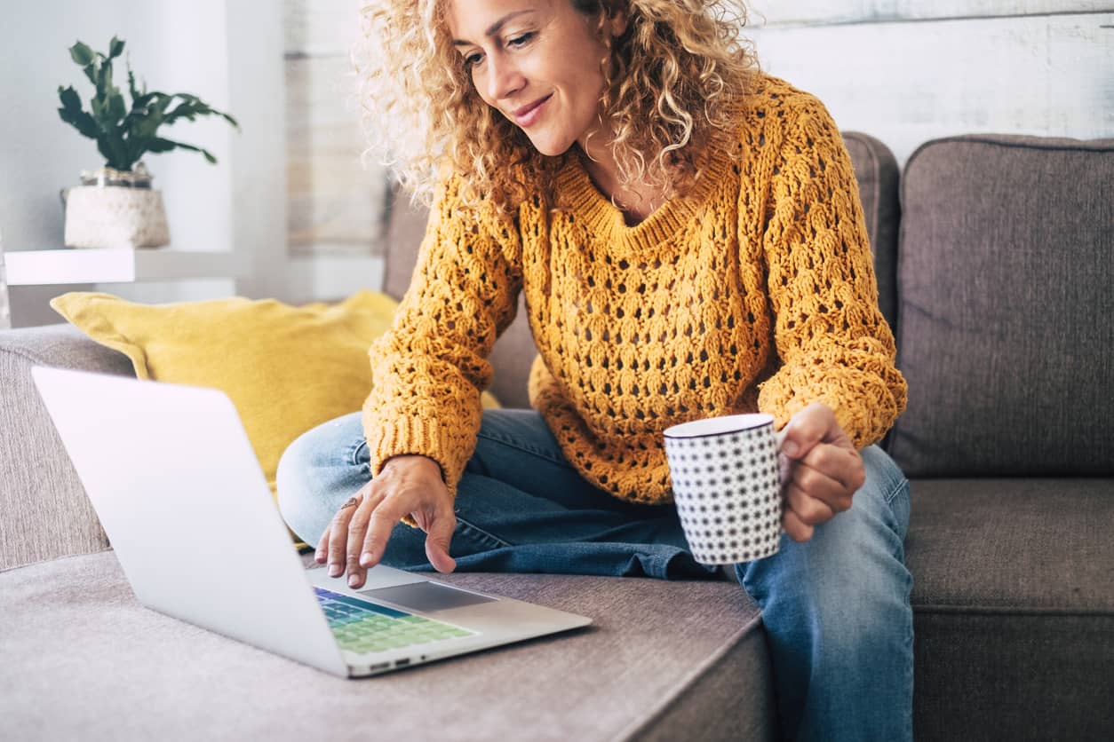 Middle age woman with curly hair working on her laptop on the sofa at home