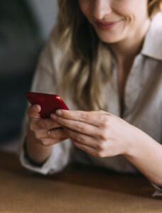 Close up photo of cheerful business woman holding red smartphone and sitting at home office desk