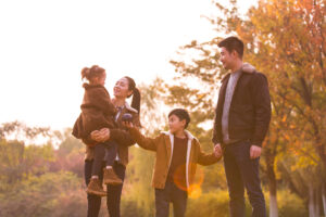 A happy young family of four by a colorful jungle at sunset in autumn, the mother holding her daughter