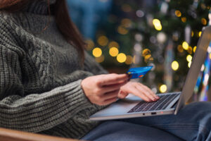 Woman holding debit card using laptop with holiday background.