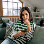 Concerned Young Woman Using Smart Phone In A Living Room
