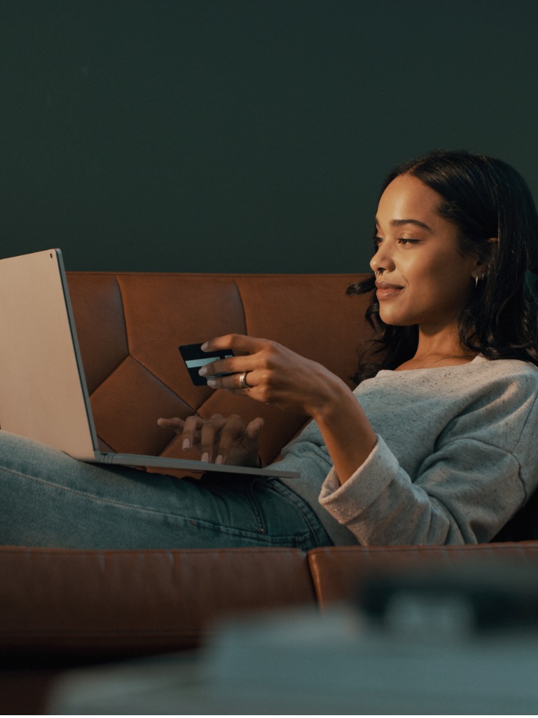 Shot of young woman using her credit card and laptop to shop online while relaxing at home.