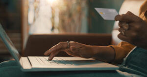 Person holding credit card while using laptop