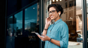 Woman standing outside and putting her earpods in to listen to take a phone call through her cellphone.