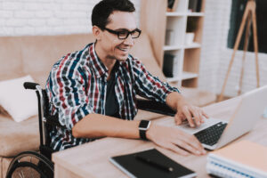 Young Disabled Man On Wheelchair Working At Home.