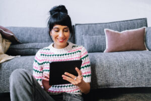 A Happy Businesswoman Sitting On The Floor In Her Living Room And Reading Something On Her Tablet