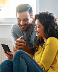 Smiling couple at home looking at their phone.