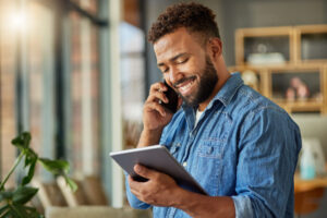 Businessman Reading An Email On His Digital Tablet. Young Freelance Entrepreneur Making S Call On His Cellphone At Home. Hispanic Businessman Working On His Wireless Device At Home
