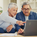Senior, Couple And Planning On Laptop In Living Room With Document For Finances, Investment Or Retirement. Elderly Man, Woman And Pointing By Technology For Online Banking, Account Balance Or Savings