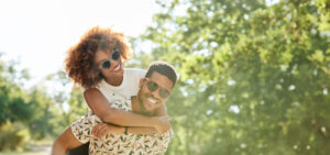 Young Couple Enjoying Piggyback Ride On Sunny Day