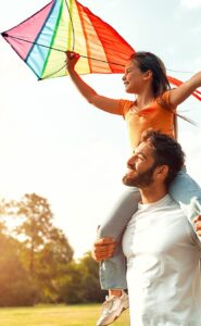 Dad with daughter on shoulders holding a kite.