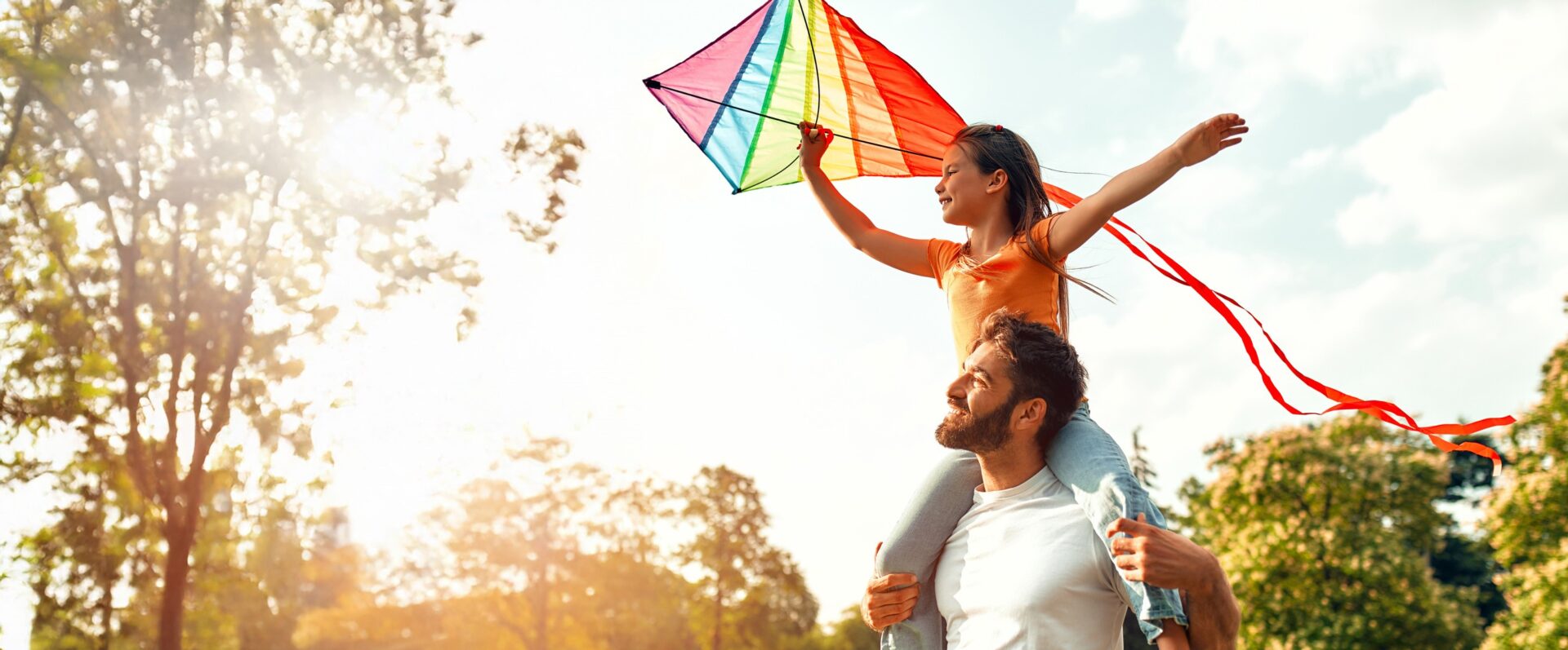 Dad with daughter on shoulders holding a kite.