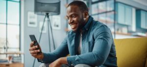Excited man sitting on couch looking at phone.
