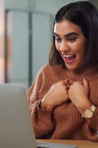 Shot of a young woman looking surprised while using a laptop at home