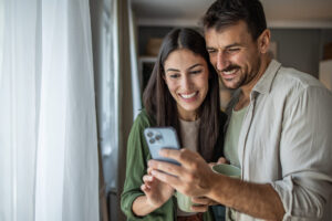 A couple drinks morning coffee and looks at their phone together