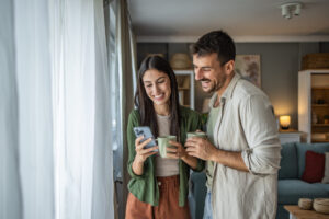 A couple drinks morning coffee and looks at phone together